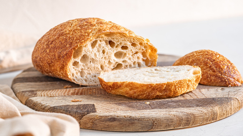 Sliced loaf of bread on a wooden cutting board with linens on the side.