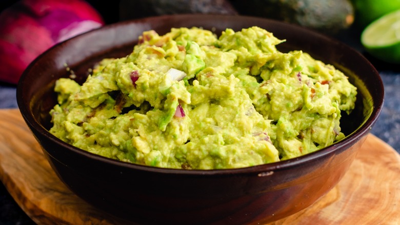 A bowl of guacamole on a wood tray