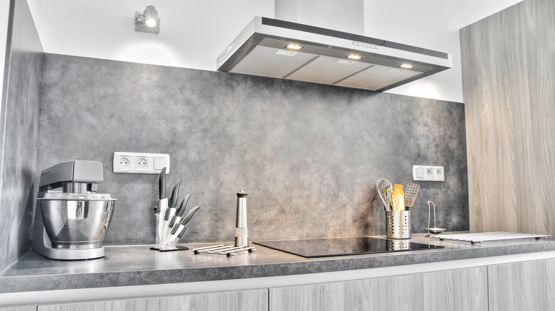 A modern, sleek luxury kitchen with marble countertops, an electric stove, and a sleek ventilation hood