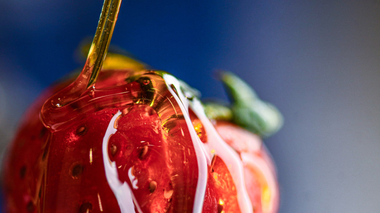 Runny honey being poured onto a strawberry in close-up against a blue background
