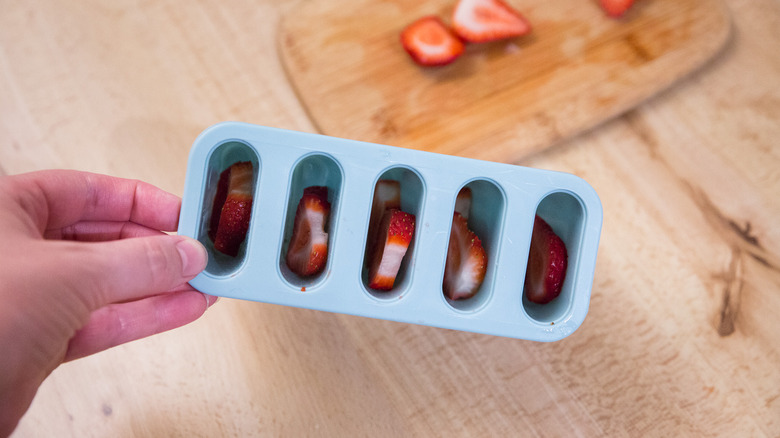 hand holding popsicle mold containing sliced strawberries