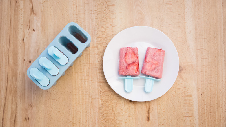 pink popsicles on white plate next to popsicle mold