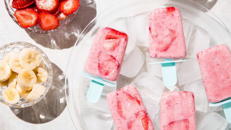 fruit popsicles served on table over ice next to bowls of bananas and strawberries