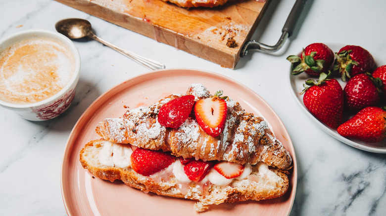 Strawberry cheesecake croissant on a pink plate besides a coffee.