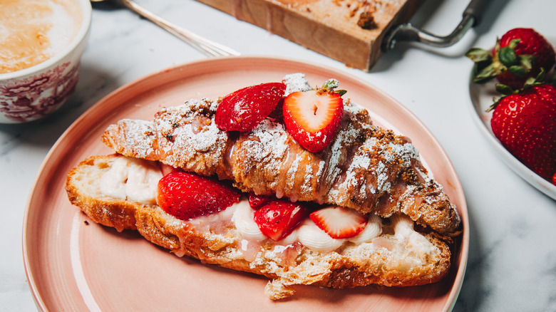 Strawberry cheesecake croissant on a pink plate besides a coffee.