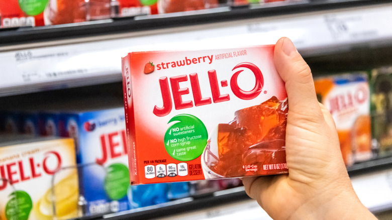 Hand holding a box of strawberry Jell-O in store aisle