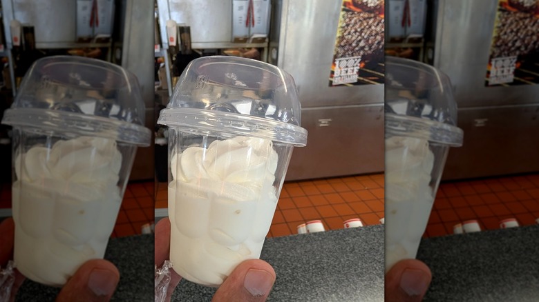 Hand holding plastic burger king cup with ice cream with kitchen in background, mirrored
