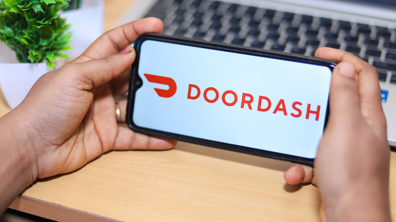 Hands holding a phone displaying the DoorDash logo