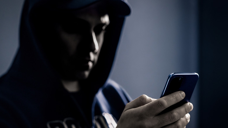 A person with a hood over their head using a cell phone in the dark
