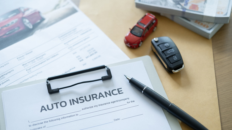 An auto insurance contract with a pen, car keys, a toy car, and banknotes