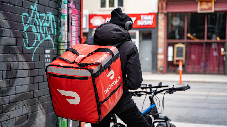 A DoorDash delivery driver on bicycle in an alley