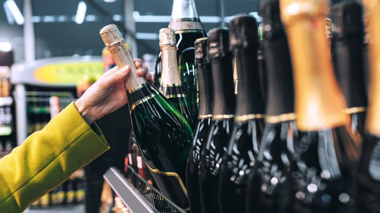 A woman taking a bottle of champagne from a store shelf