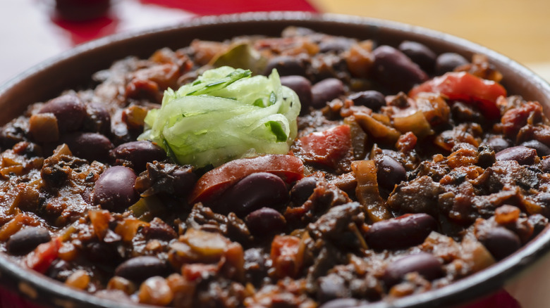 Close up on a part of vegetarian chili showing off the beans and tomatoes with a fresh green garnish