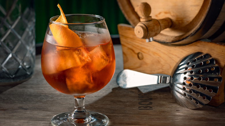 Barrel aged negroni next to strainer and barrel.