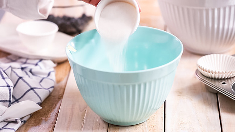Pouring sugar into a bright blue mixing bowl.