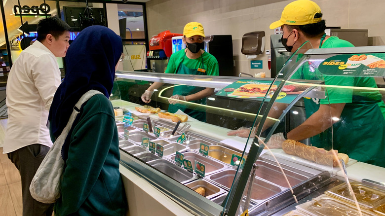 Customers standing in front of glass at Subway counter