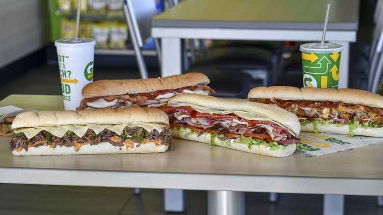 four foot-long Subway sandwiches and drinks sitting on a table at one of the chain's restaurants
