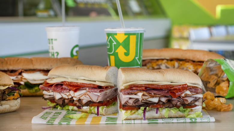 Subway sandwiches cut in half and displayed on a restaurant table with drink cups and chips