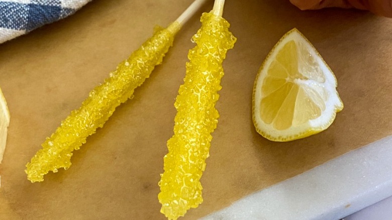 Two sticks of homemade lemon flavored rock candy on parchment paper