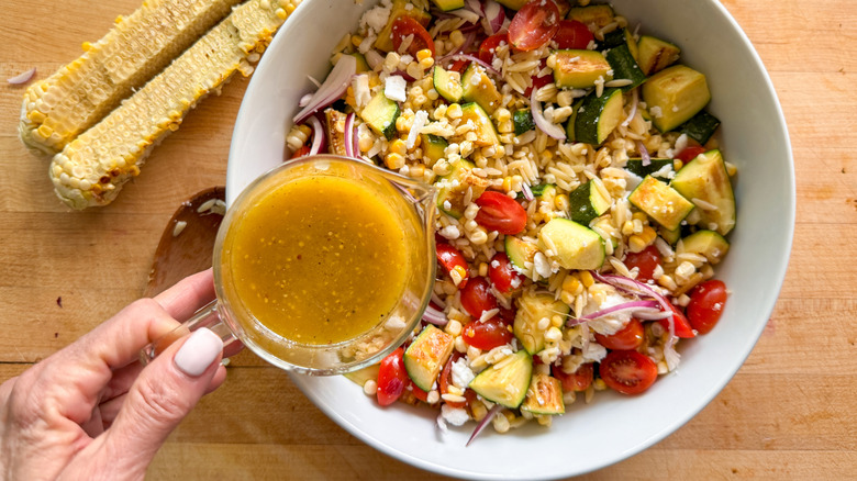 hand adding dressing to pasta salad
