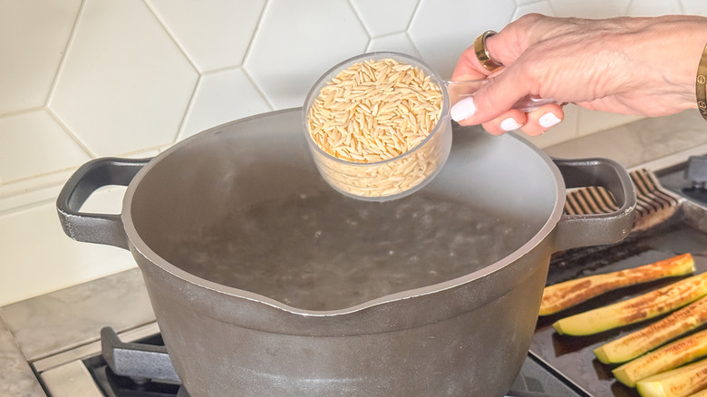 hand adding orzo to pot