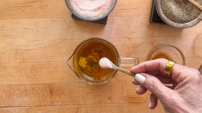 hand adding salt to bowl with dressing ingredients