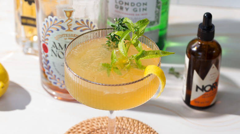 Side view of yellow cocktail next to lemon verbena and lemon and liqueur bottles