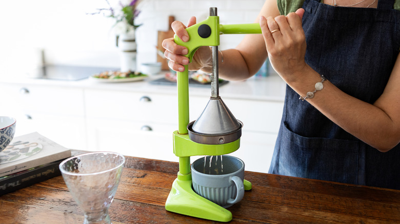A woman in an apron using a green manual countertop juicer in her kitchen