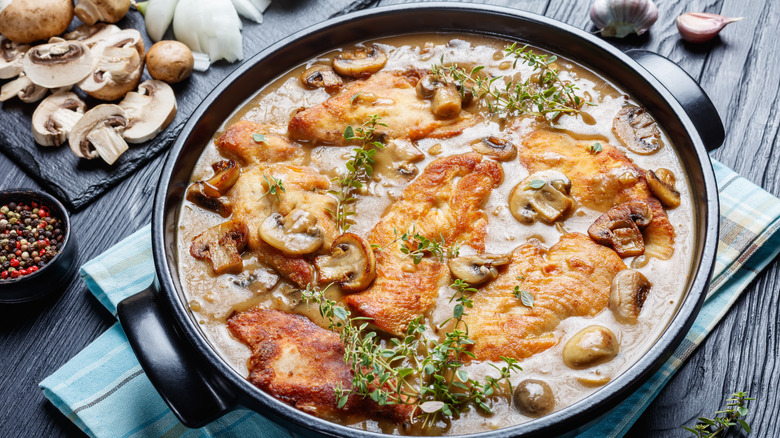 chicken marsala in a large round pan on a wood surface iwith fresh mushrooms, garlic, and onion