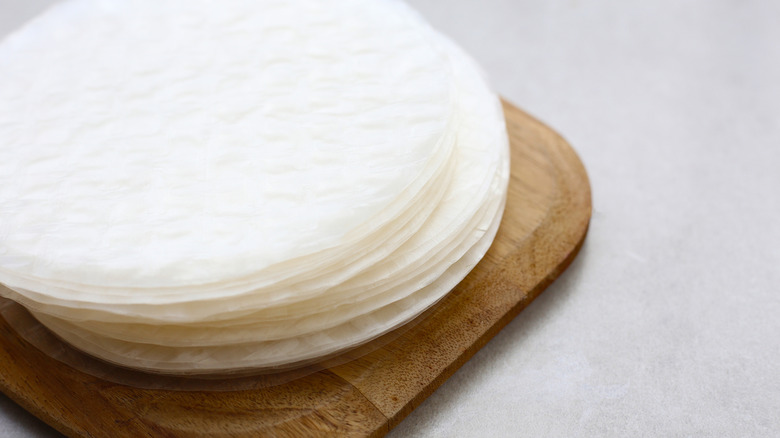 A stack of round rice paper sheets atop a wooden cutting board