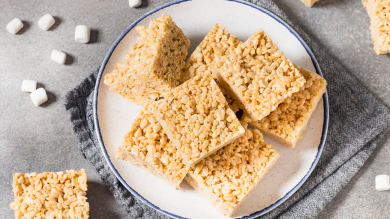 Squares of Rice Krispie Treats on white plate next to miniature marshmallows