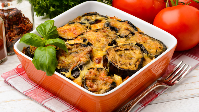 A pan of moussaka with a fork and some tomatoes