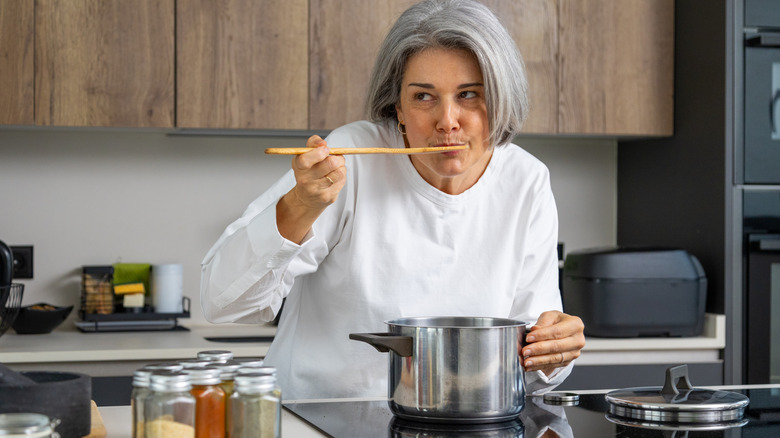 Senior woman tasting soup with a wooden spoon in a modern kitchen