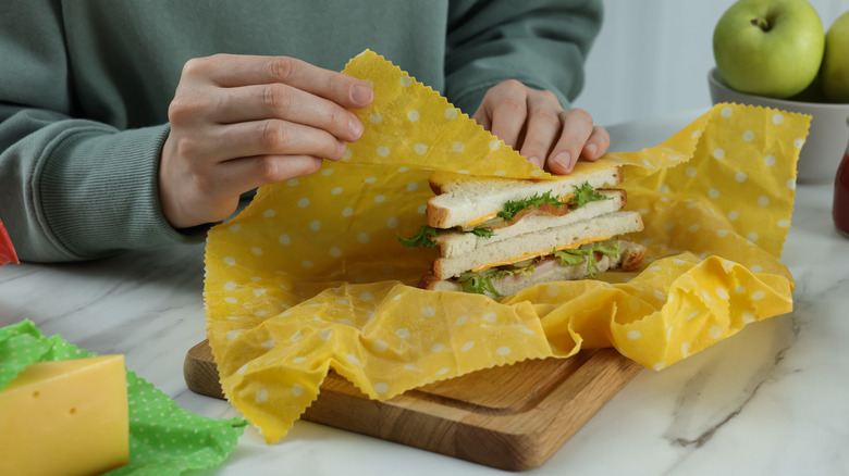 Woman packing sandwich into beeswax food wrap at white marble table