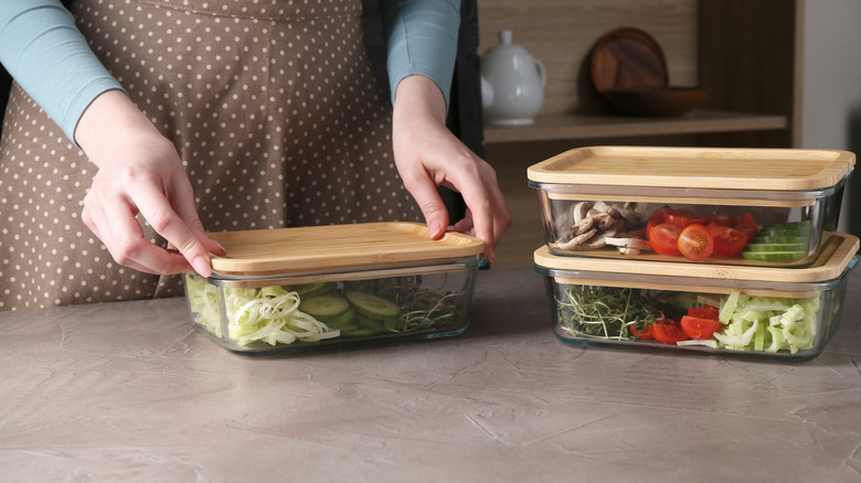 Woman closing glass containers with fresh vegetables at grey table