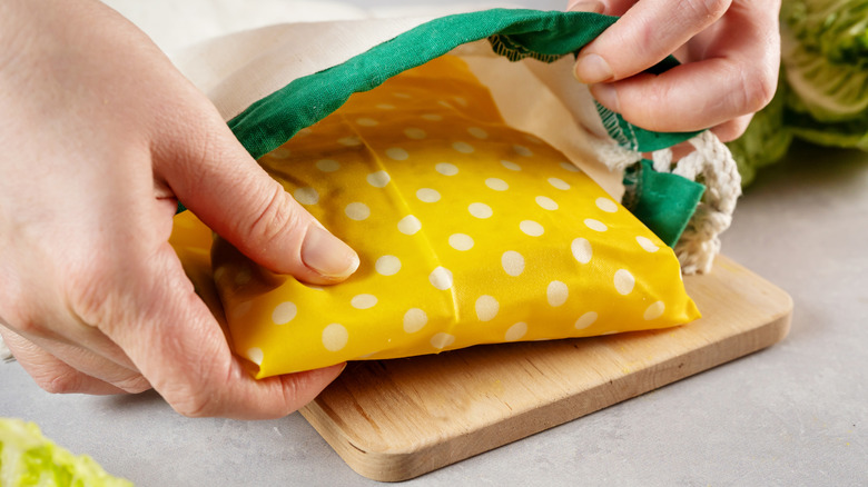 Woman hands placing sandwich wrapped in beeswax cloth into cotton bag