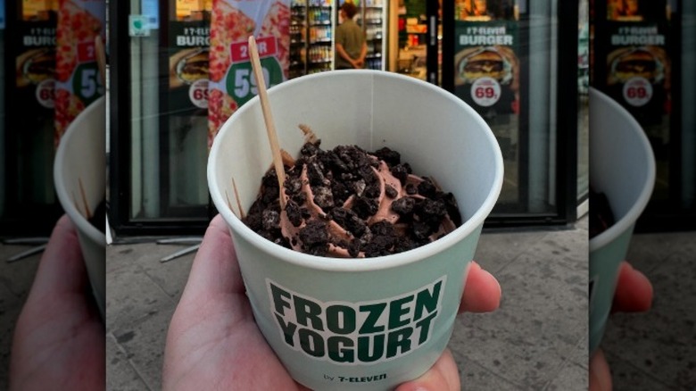 Hands holding a cup of 7-Eleven frozen yogurt with cookie crumbs