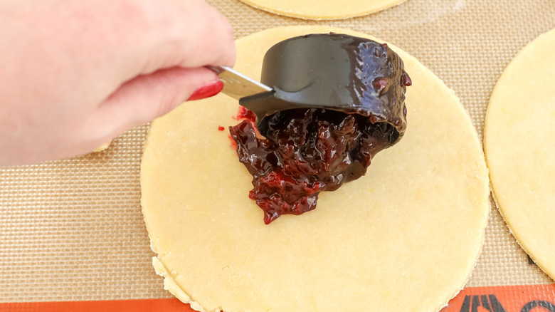 cherry pie filling being put on empanada dough