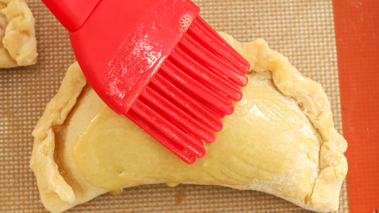 empanada dough being brushed with an egg wash