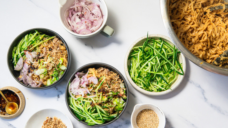 Two bowls of spicy peanut noodles with all the toppings around