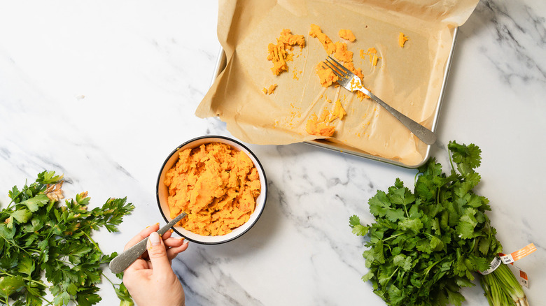 Bowl of mashed sweet potato next to baking sheet