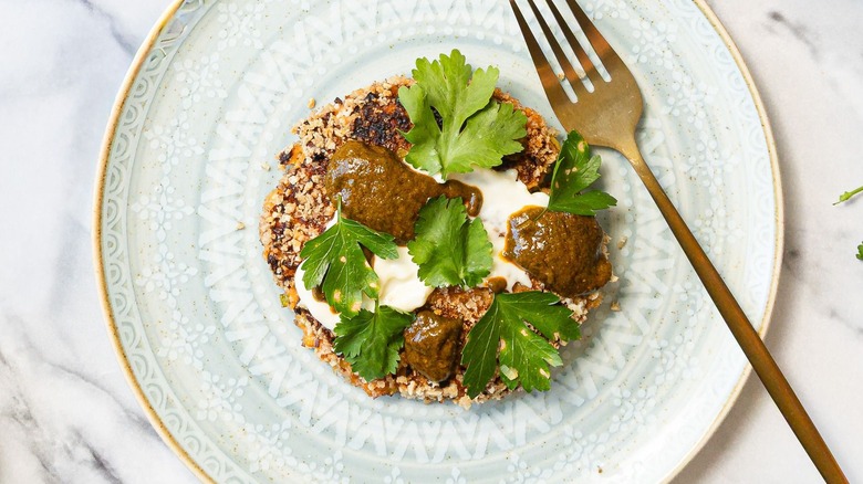Crab cake on plate with mayonnaise, chermoula, and herbs