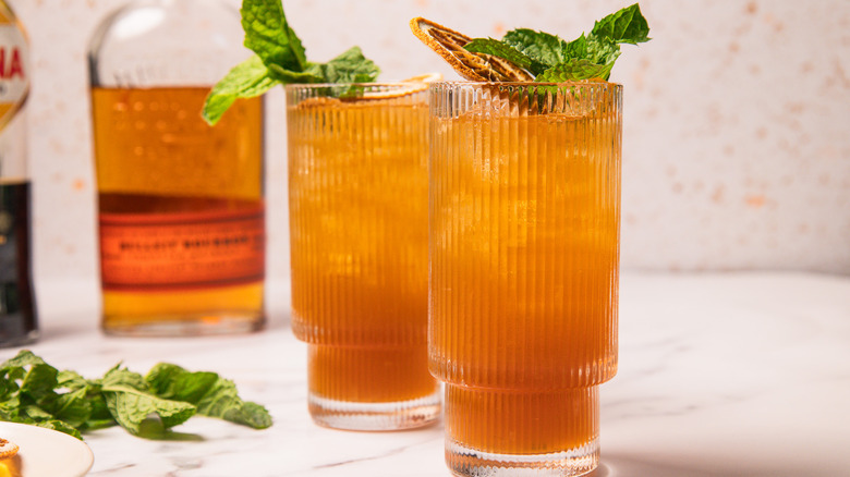 Two glasses of sweet tea whiskey smash with bourbon in background