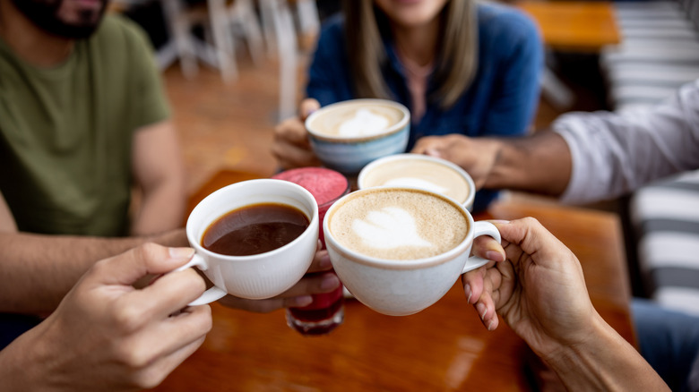 View of group of friends toasting mugs of coffee and cafe drinks