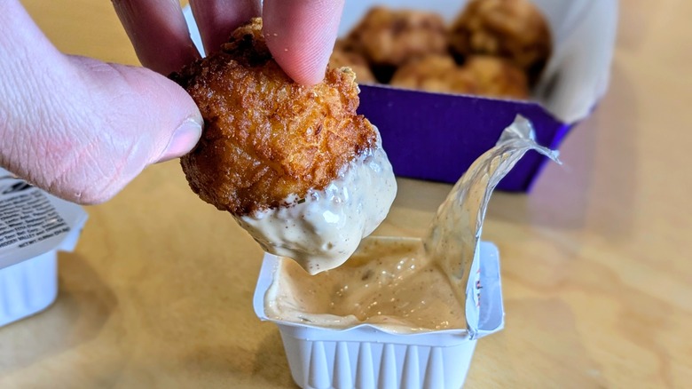 A close-up of a hand dipping a chicken nugget into spicy ranch
