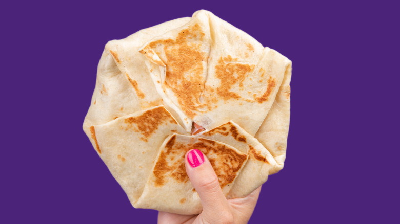 Hand holding Taco Bell Crunchwrap Supreme in purple background