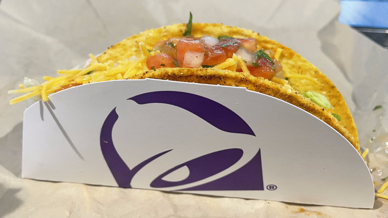 A single taco in a Taco Bell cardboard holder sits on a table.