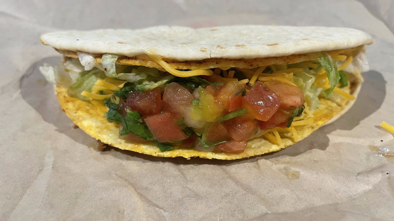 A flatbread wrapped taco sits on a crinkled paper wrapper.