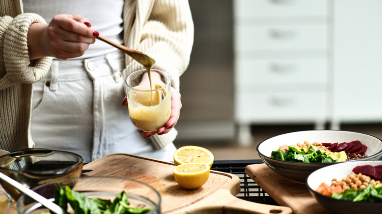 A person drizzles tahini in a cup near some cut lemons and salads