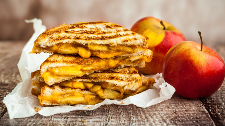 Grilled cheese sandwiches with apple cut in half and stacked up next to two whole red apples
